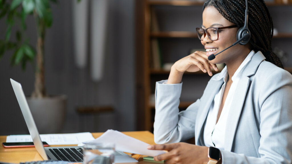 Young smiling Black businesswoman in headset working remotely from home during maternity leave, selective focus. Pleasant black female remote recruiter communicating with candidates online